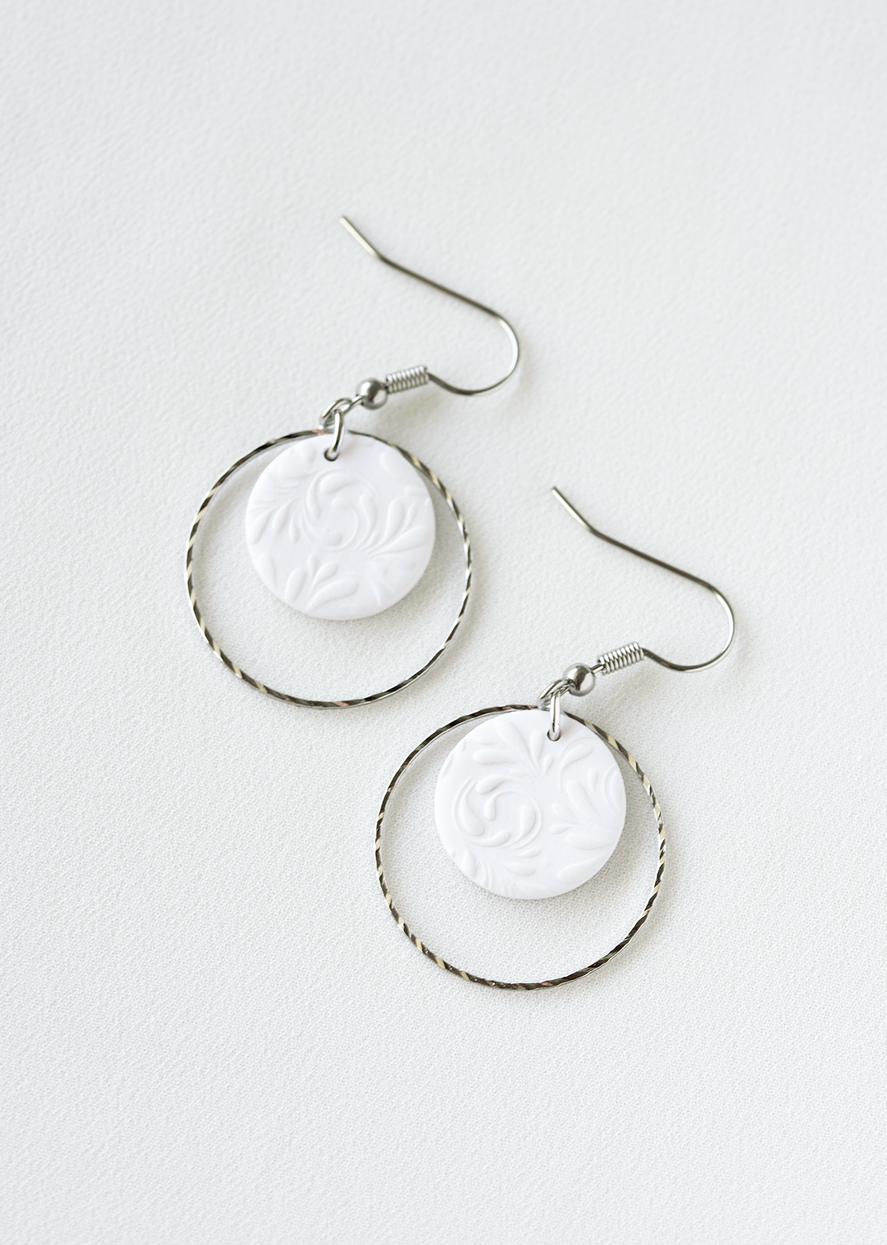 Pair of stainless steel earrings with white polymer clay pendant.