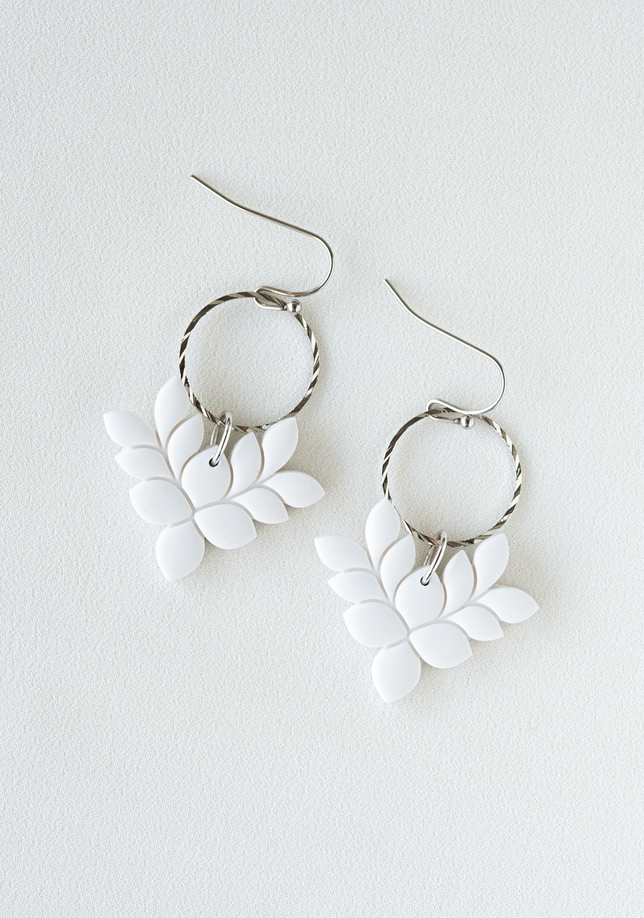 White leaf-shaped polymer clay earrings with gold pated stainless steel hooks on a white background.