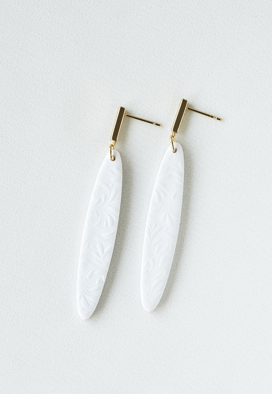 White dangle earrings with gold posts on a light gray background