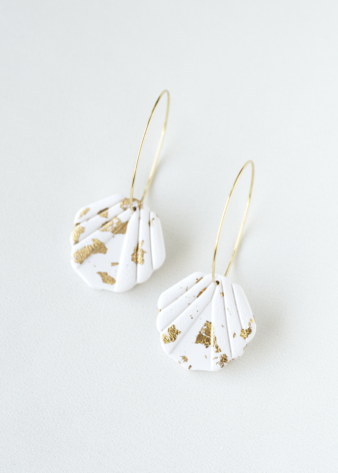 Pair of white hoop earrings with gold accents on a light gray background.