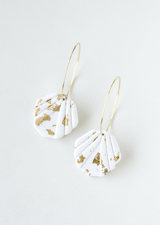 Pair of white hoop earrings with gold accents on a light gray background.