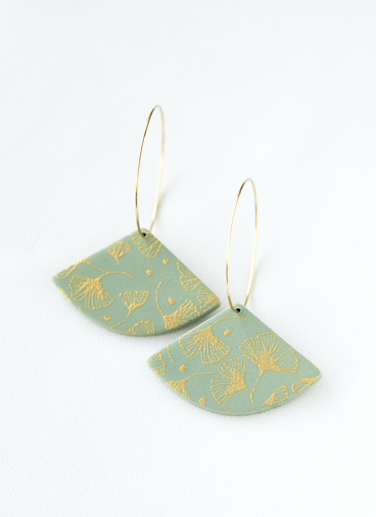 Green polymer clay hoop earrings with gold patterns on a white background