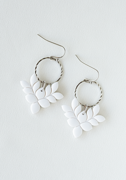 White leaf-shaped polymer clay earrings with gold pated stainless steel hooks on a white background.